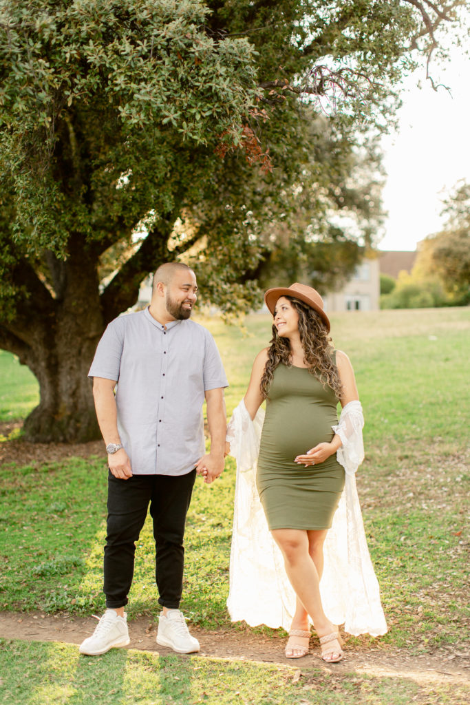 Couple holding hands and smiling at each other while woman holds pregnant belly