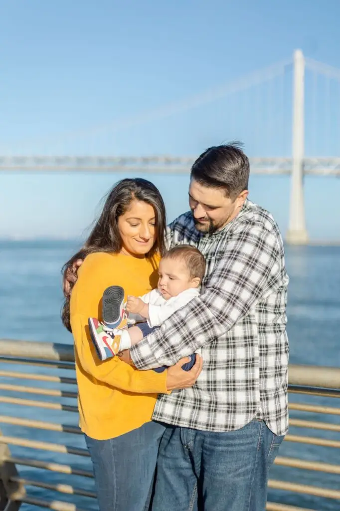Samita, Scott, and baby Paul strolling along the Embarcadero as a family with the Bay Bridge standing tall in the background.