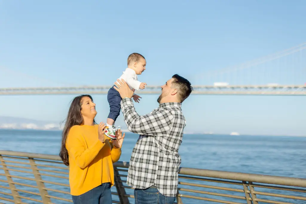 Samita, Scott, and baby Paul strolling along the Embarcadero as a family with the Bay Bridge standing tall in the background.